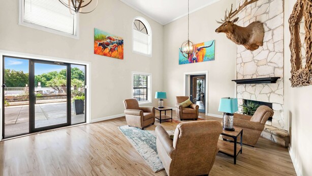 A spacious living room with a stone fireplace, large windows, and a mounted deer head. - Best Western George West Executive Inn (George West)