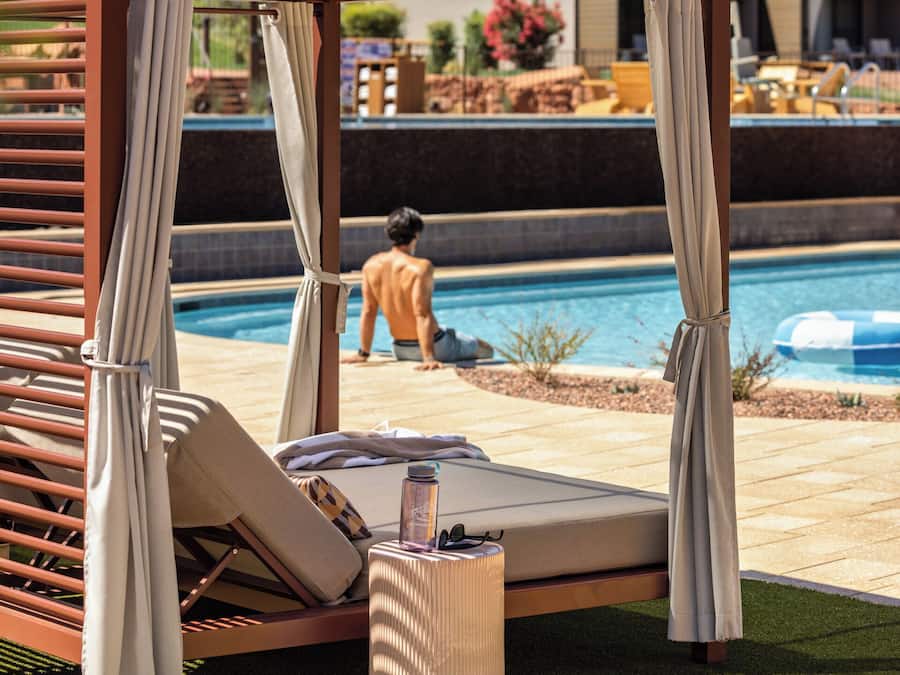A poolside lounge area with a canopy, a sunbed, and a small table with a bottle.