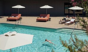 A swimming pool with lounge chairs and umbrellas, a person swimming, and a building in the background. - Outbound Sedona (Sedona)