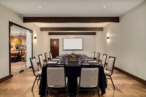 A conference room with a long table, chairs, a projector screen, and a small plant centerpiece.