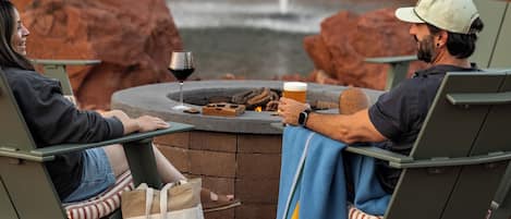 Two people seated at a round table with a drink and a glass of wine, with a fire pit and a waterfall in the background.