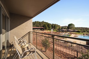 A balcony with a pool, lounge chairs, and a view of a landscaped area with a fountain.