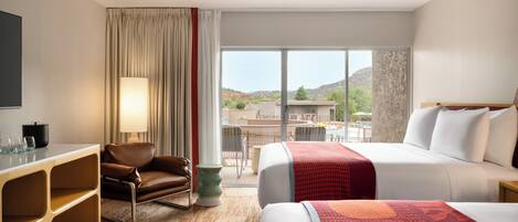 A hotel room with a bed, a desk, a chair, a lamp, and a view of the outside.
