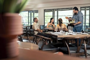 Un restaurante con una decoración moderna, ventanas amplias y un camarero atendiendo a los clientes.