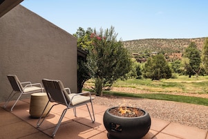 An outdoor patio with two chairs and a fire pit, overlooking a landscaped garden and a hilly landscape.