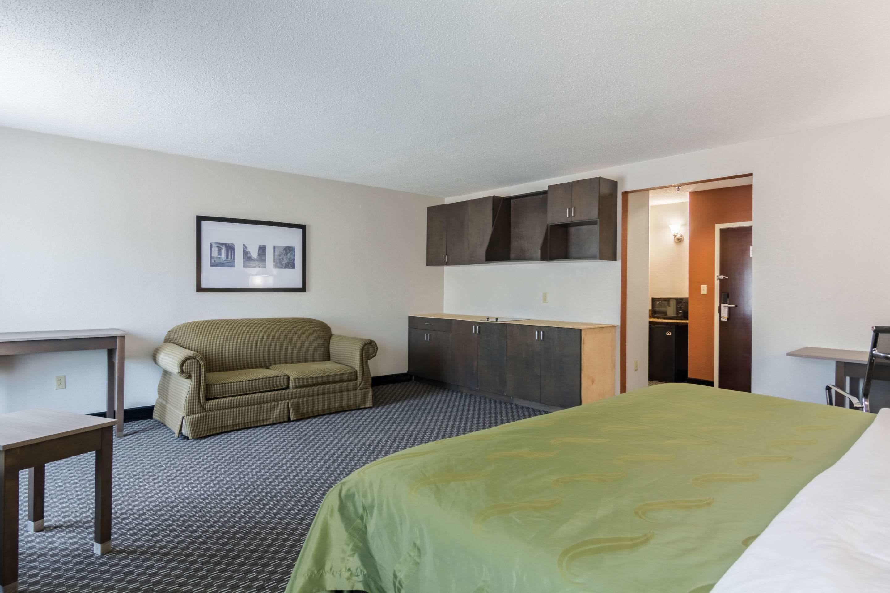 A hotel room with a bed, a sofa, a desk, and a kitchenette.