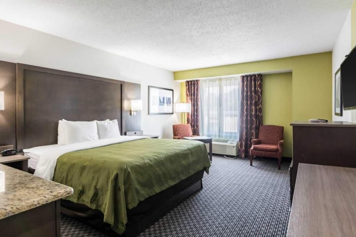 Ein Hotelzimmer mit Bett, Schreibtisch, Stuhl und einem Vorhangfenster.