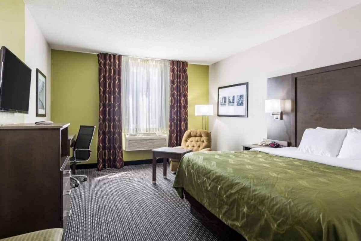 Ein Hotelzimmer mit Bett, Schreibtisch, Stuhl, Fernseher und einem fensterbepflanzten Fenster.
