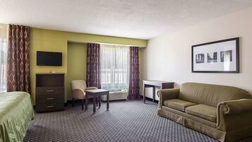 A hotel room with a bed, a desk, a sofa, a chair, a TV, and a framed picture on the wall.