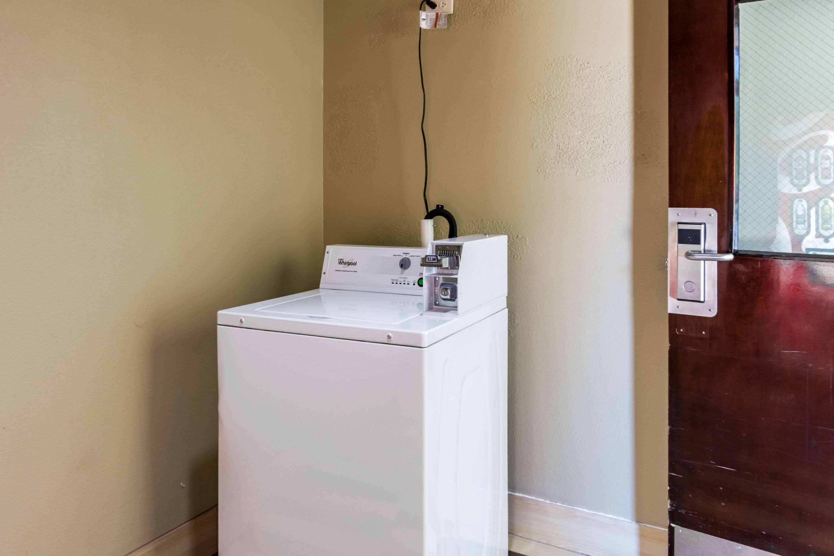 A compact, white Whirlpool washer and dryer unit against a beige wall, with a wooden door to the right.
