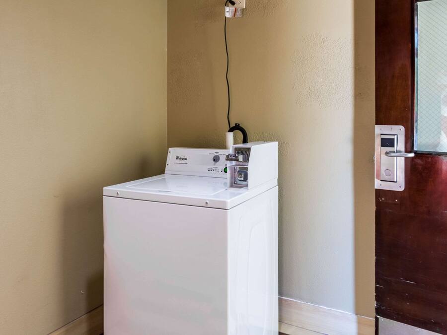 Una unidad compacta de lavadora y secadora Whirlpool blanca, frente a una pared color beige, con una puerta de madera a la derecha.