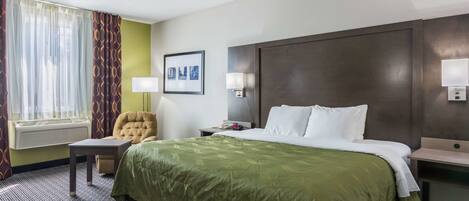 A hotel room with a large bed, a chair, a desk, and a window with curtains.
