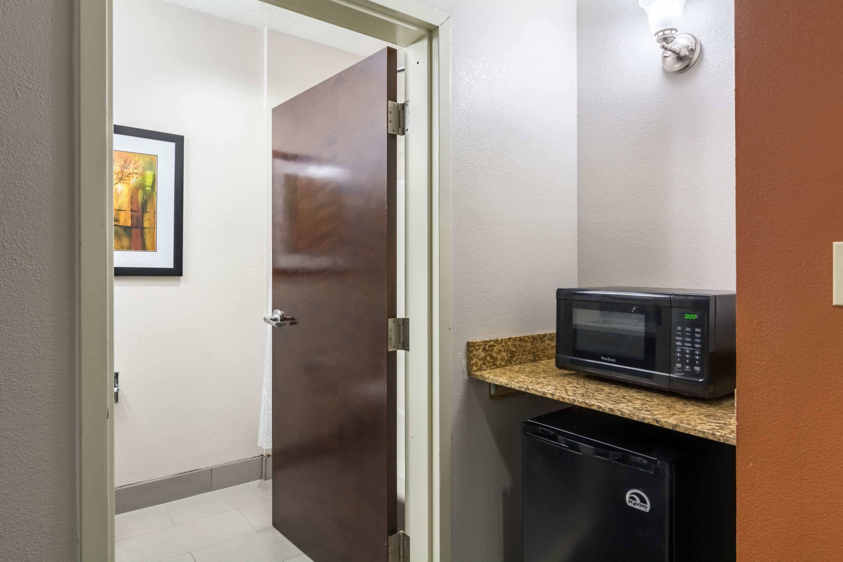 A hallway with a microwave on a countertop, a refrigerator, and a door leading to another room.