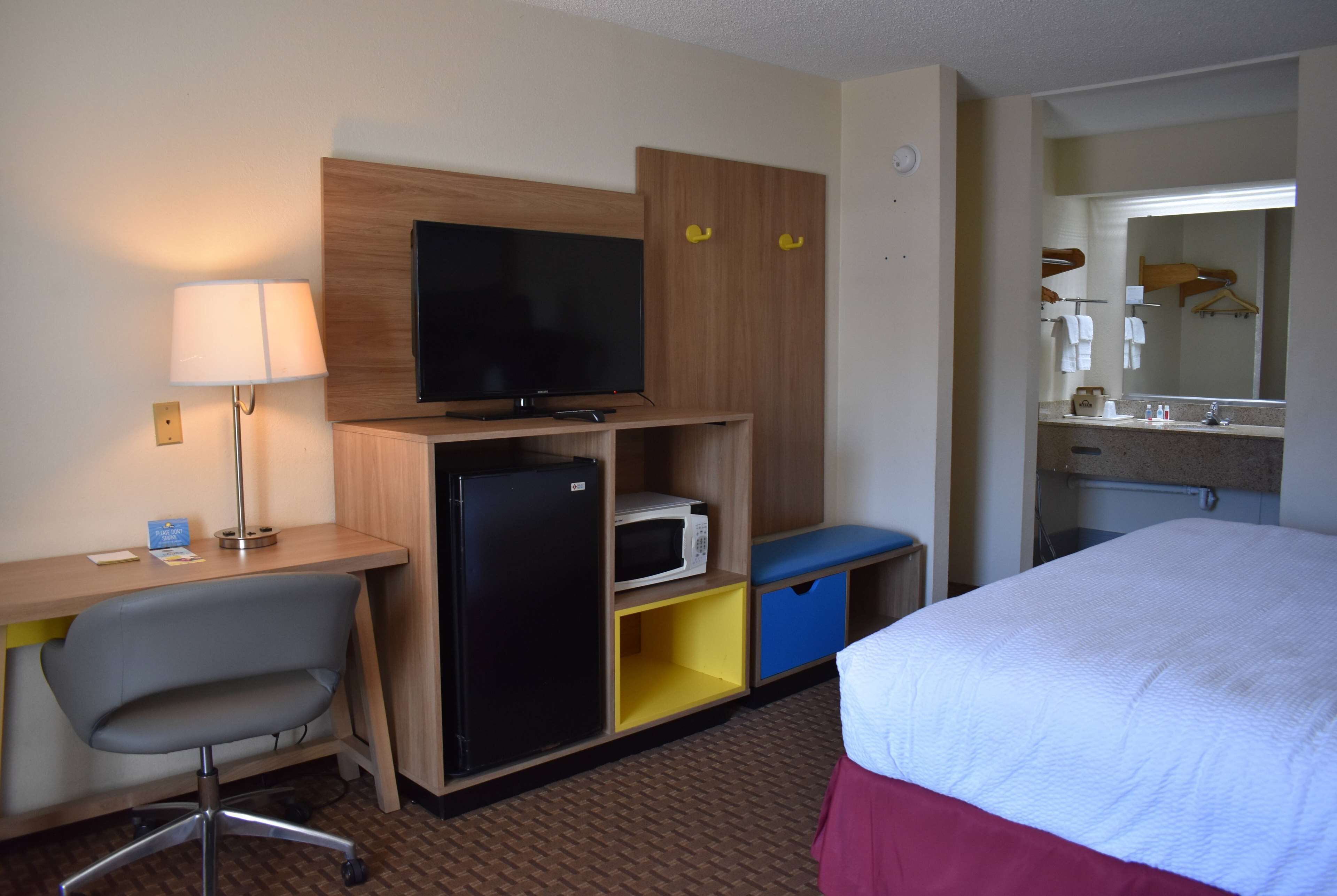 Habitación de hotel con cama, escritorio con silla, televisor, microondas y armario.