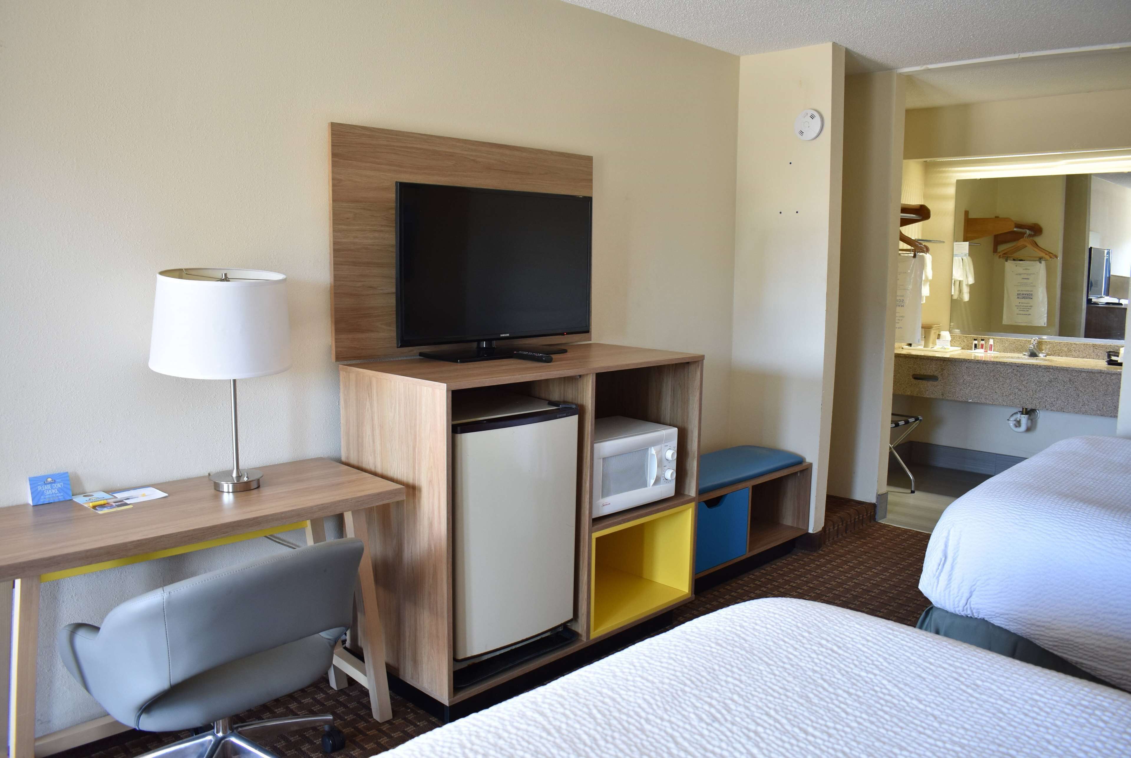 A hotel room with a desk, a television, a microwave, a refrigerator, a chair, and two beds.