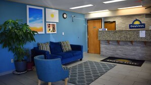 A reception area with a blue sofa, a chair, a potted plant, and a reception desk with a 'Days Inn' sign. - Days Inn by Wyndham Reidsville (Reidsville)