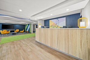 A modern reception area with a wooden reception desk, a flat-screen TV, and a seating area with yellow chairs. - Spark by Hilton Milford Boston (Milford)