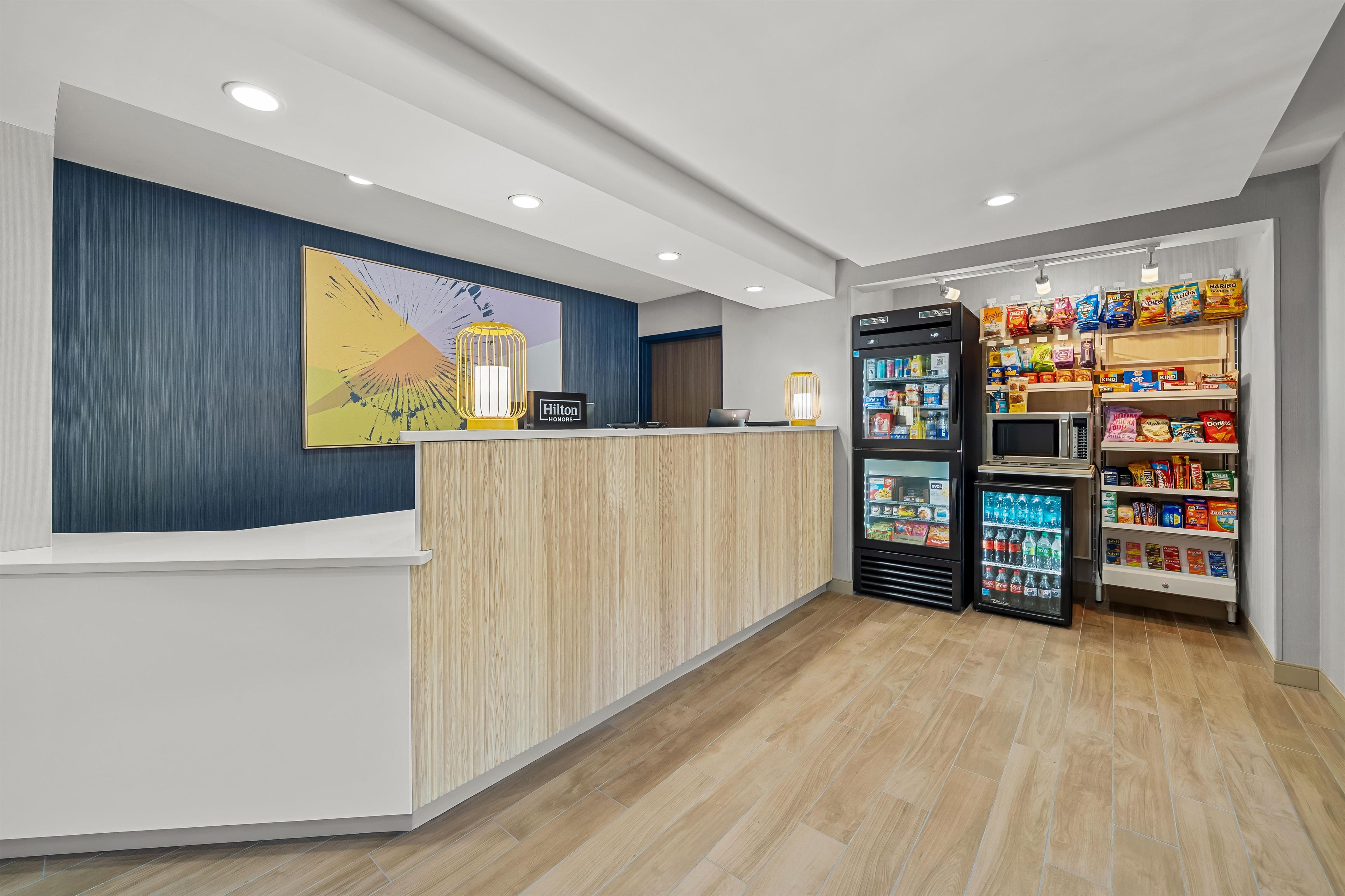 A hotel reception area with a counter, a reception desk, a refrigerator, and a snack vending machine.