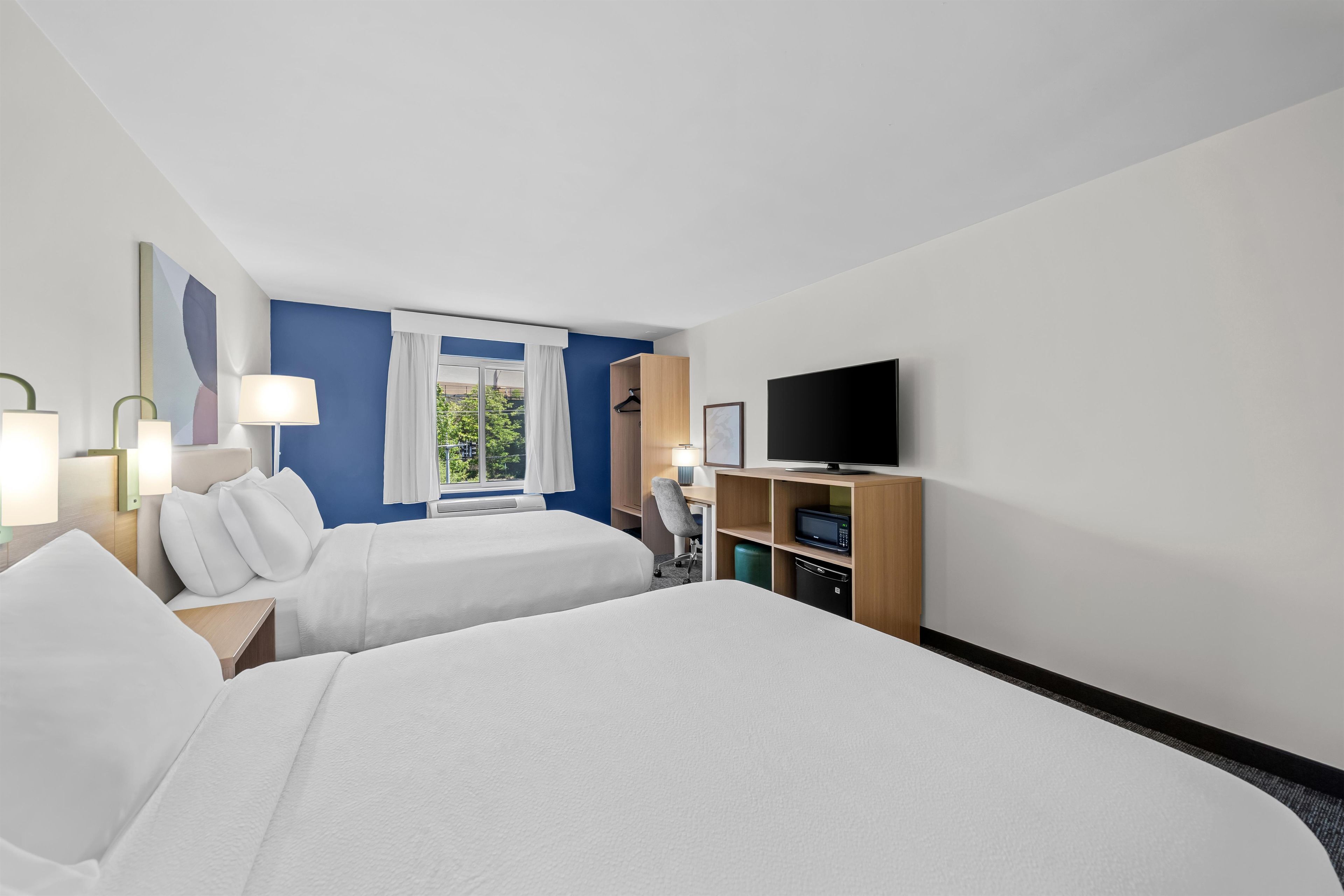 Een hotelkamer met twee bedden, een televisie, een bureau met een computer en een raam met gordijnen.
