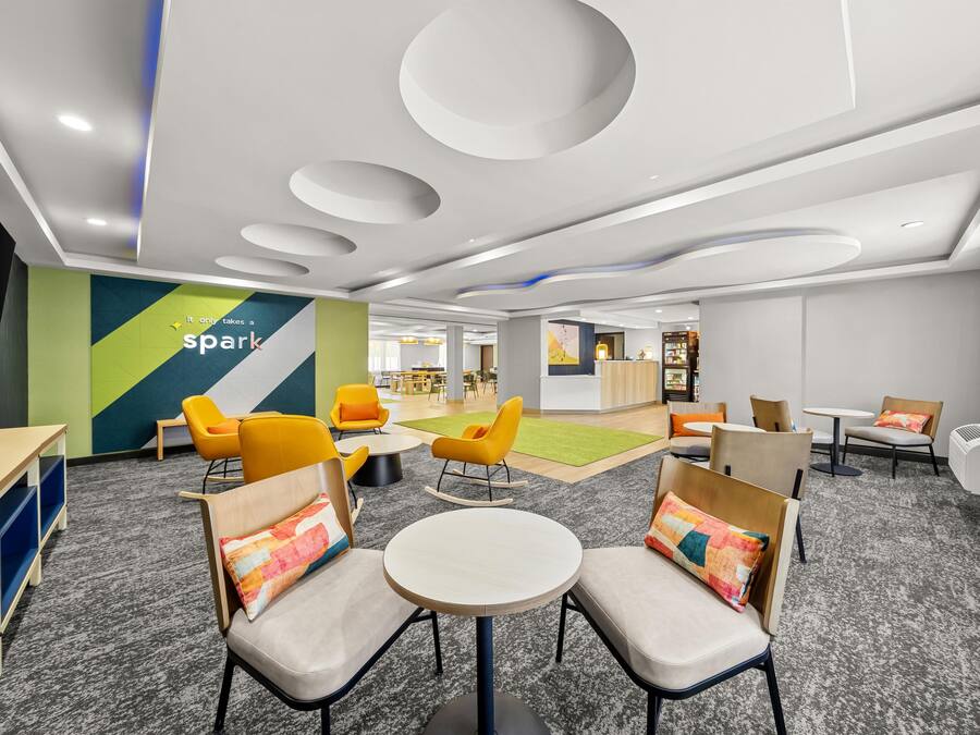 A modern lounge area with round tables and chairs, a children's play area, and a reception desk in the background.