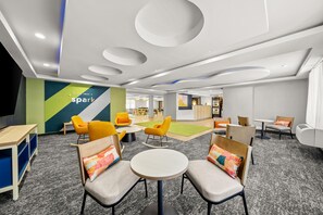 A modern lounge area with round tables and chairs, a children's play area, and a reception desk in the background. - Spark by Hilton Milford Boston (Milford)