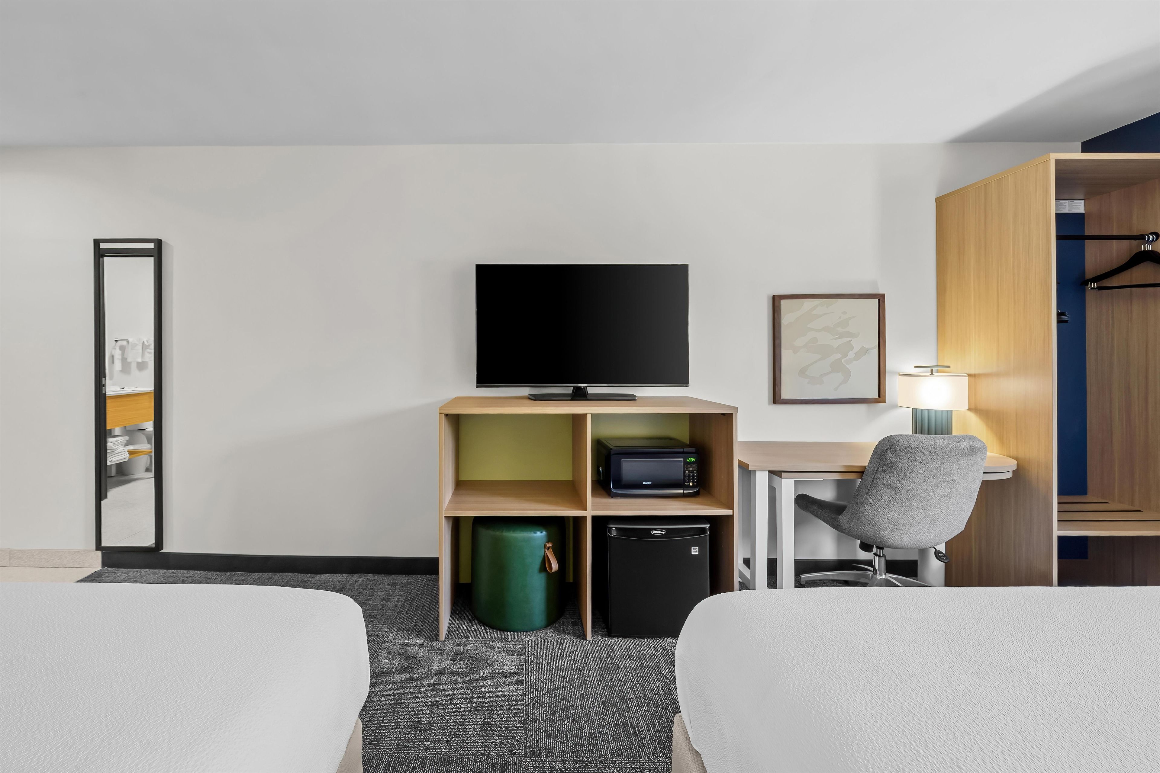 Habitación de hotel con dos camas, un escritorio con silla, televisor, microondas, cubo de basura y armario.