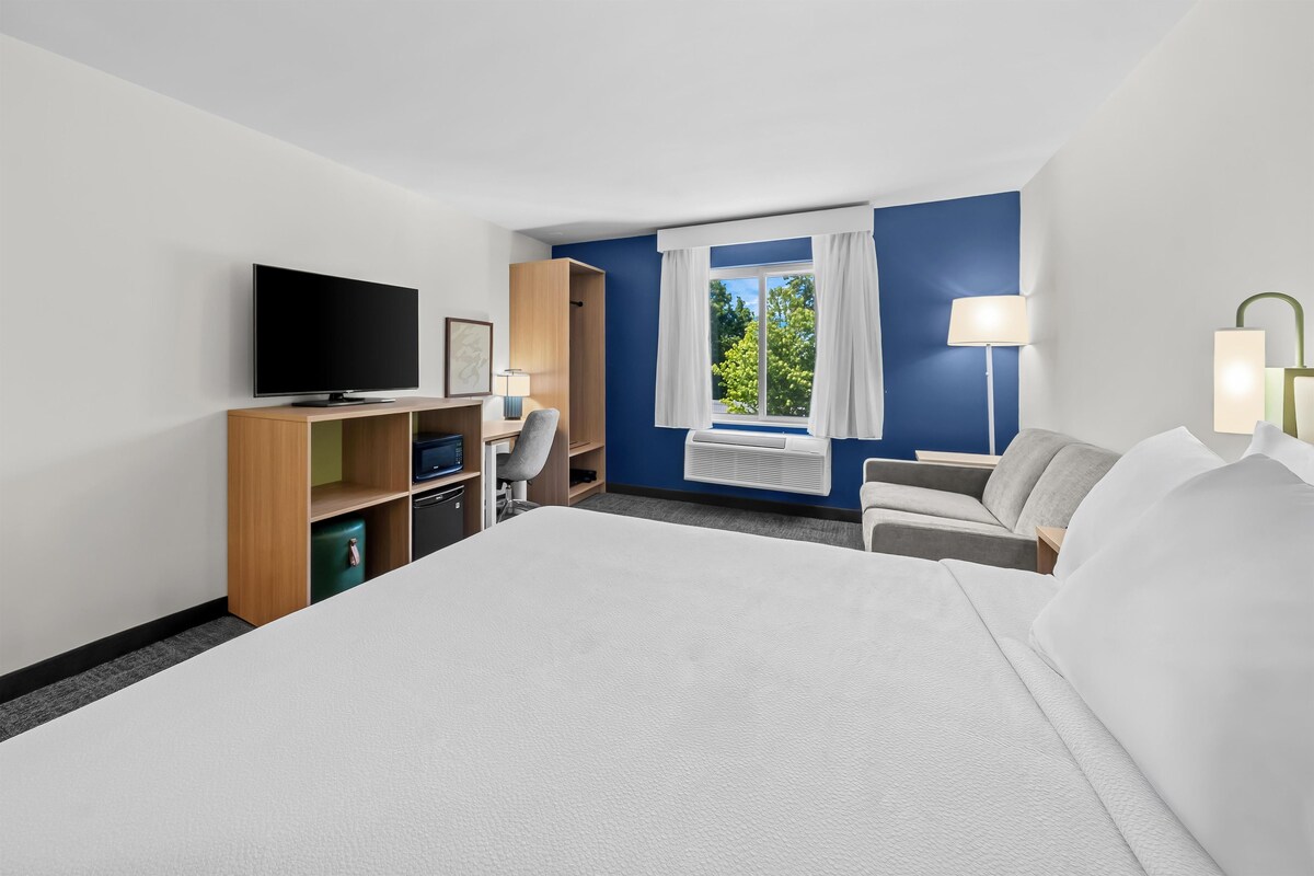 Une chambre d’hôtel comprenant un lit, une télévision, un bureau avec une chaise, une armoire, une fenêtre avec des rideaux et une lampe.