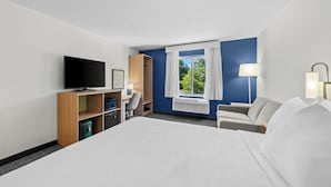 A hotel room with a large bed, a television, a desk with a chair, a wardrobe, and a window with curtains. - Spark by Hilton Milford Boston (Milford)