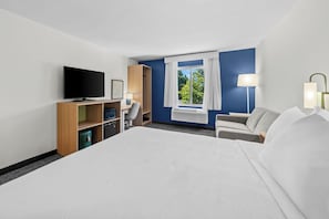 Ett hotellrum med en stor säng, en tv, ett skrivbord med en stol, en garderob och ett fönster med gardiner.