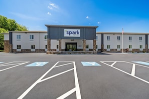 A hotel entrance with a sign reading 'spark by Hilton,' parking spaces with accessibility symbols, and a flagpole with an American flag.