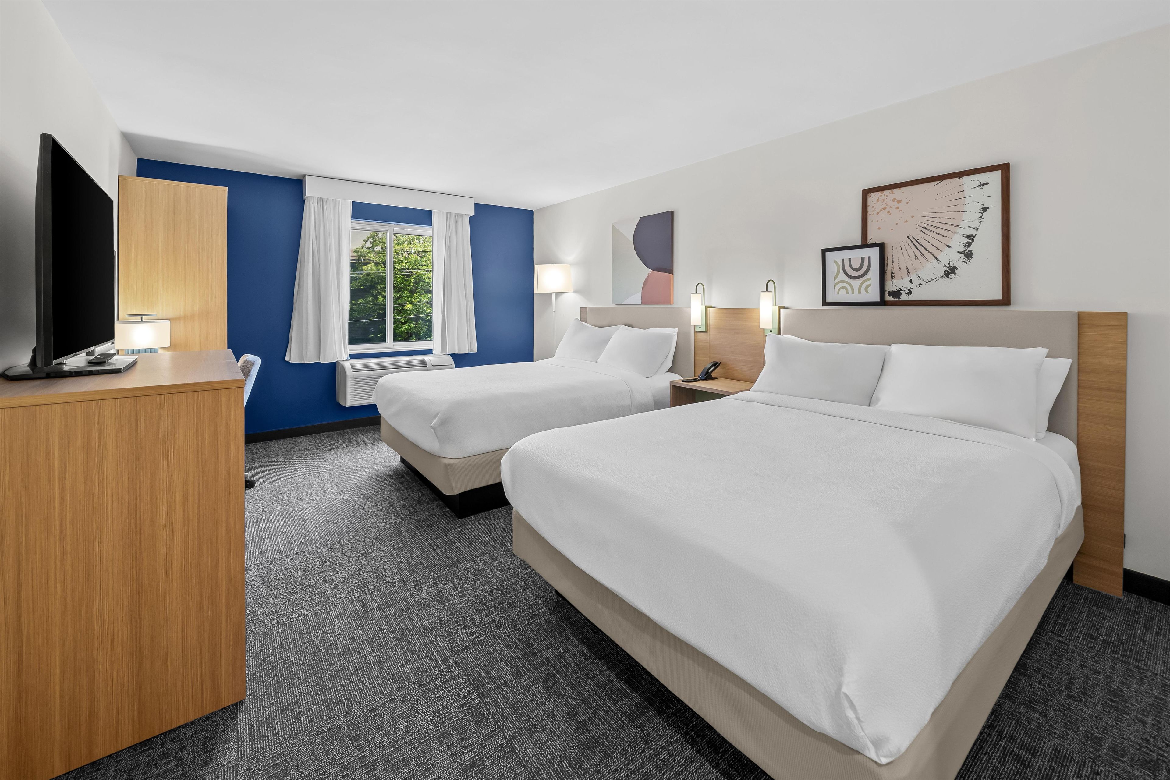 Une chambre d’hôtel avec deux lits, un bureau, une télévision et une fenêtre avec des rideaux.