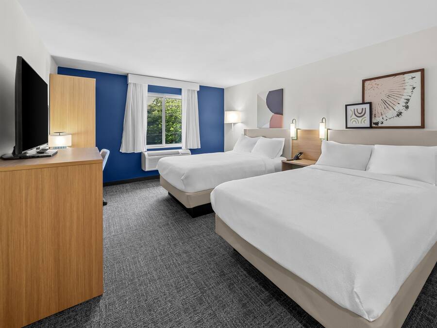 Une chambre d’hôtel avec deux lits, un bureau, une télévision et une fenêtre avec des rideaux.
