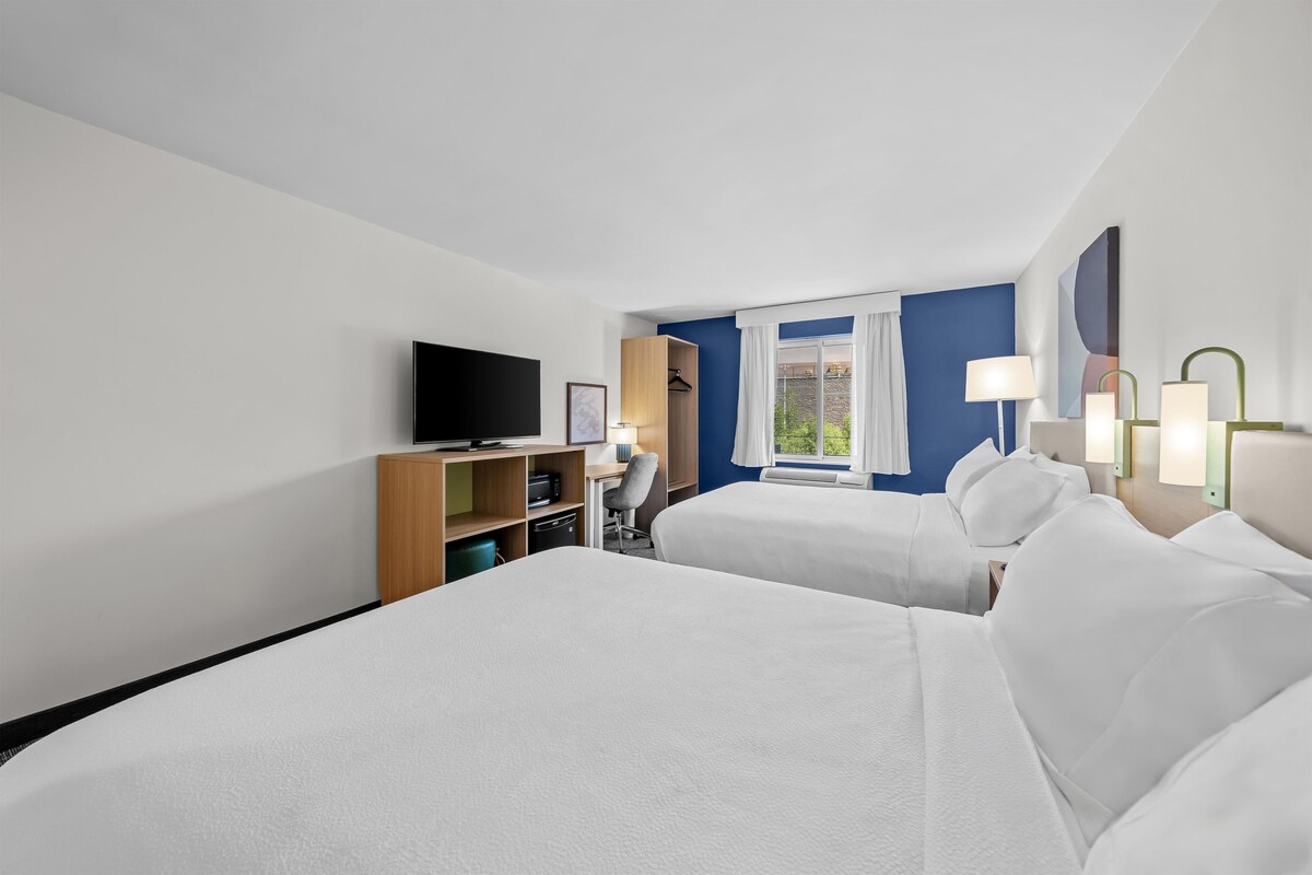Une chambre d’hôtel avec deux lits, un bureau, une télévision et une fenêtre avec des rideaux.