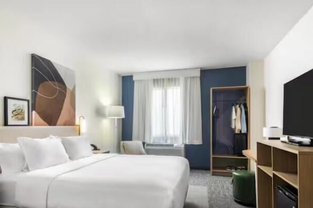 Ett hotellrum med en säng, ett nattduksbord, en lampa, en garderob och en tv.
