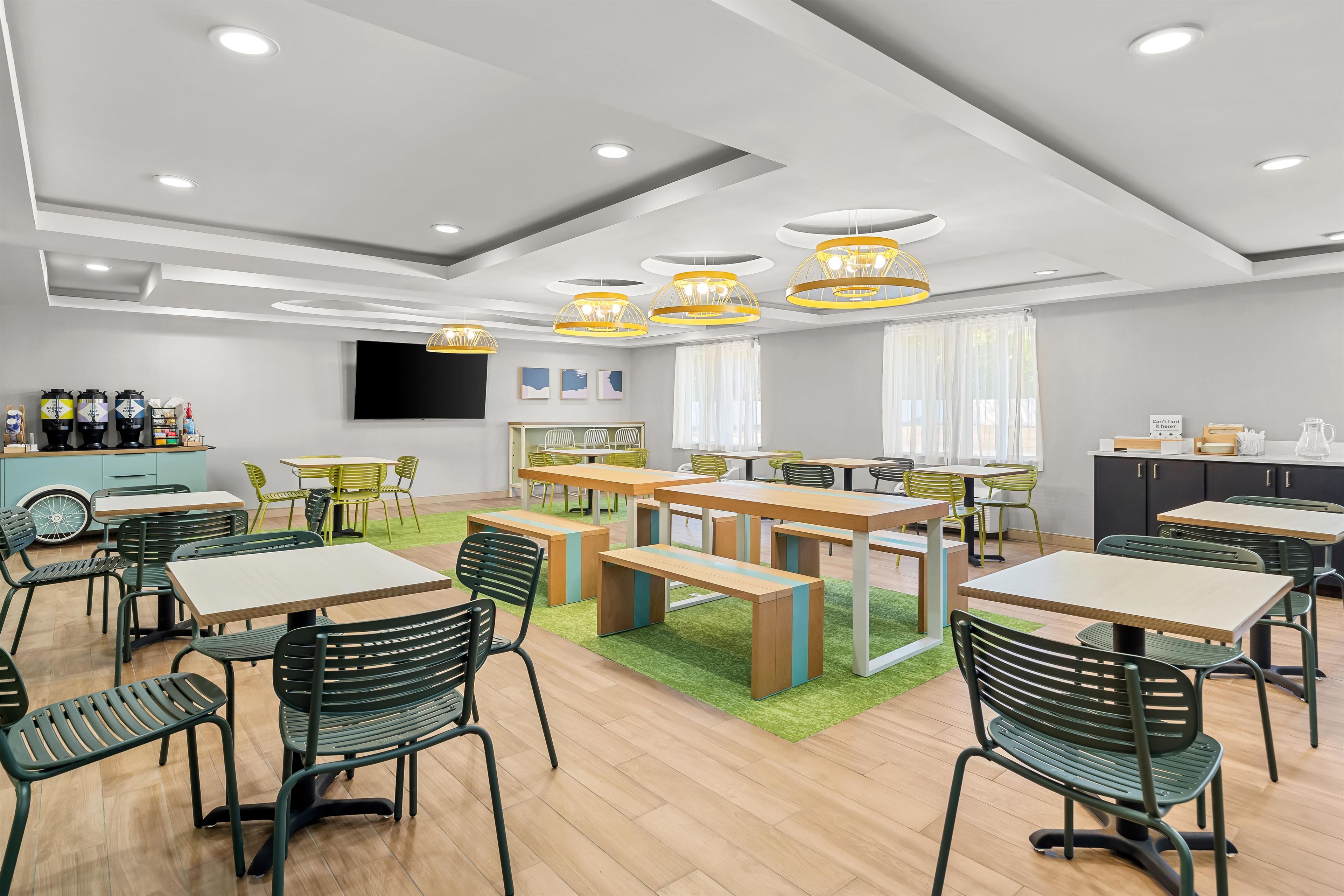 A modern dining area with multiple tables and chairs, a flat-screen TV, and a bar area with bottles.