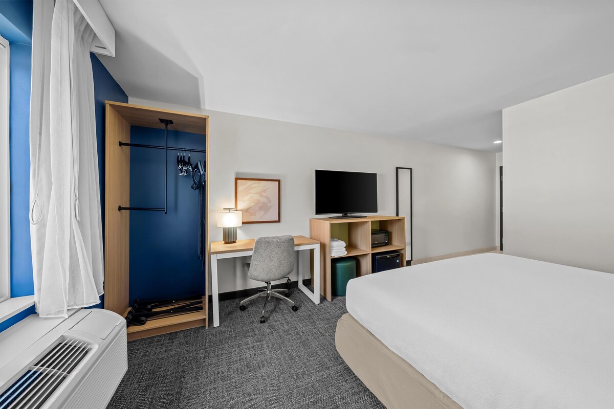Une chambre d’hôtel équipée d’un lit, d’un bureau, d’une chaise, d’une télévision et d’une fenêtre avec des rideaux.
