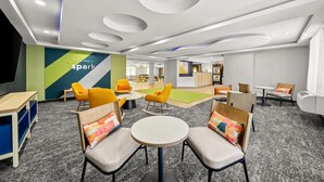 Un'area lounge moderna con tavoli e sedie rotonde, uno spazio giochi per bambini e, sullo sfondo, un banco reception.