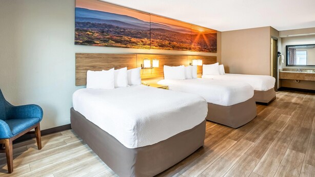 Ein Hotelzimmer mit zwei Betten, einem Schreibtisch, einem Stuhl und einem großen Wandbild mit einer Landschaftsdarstellung.