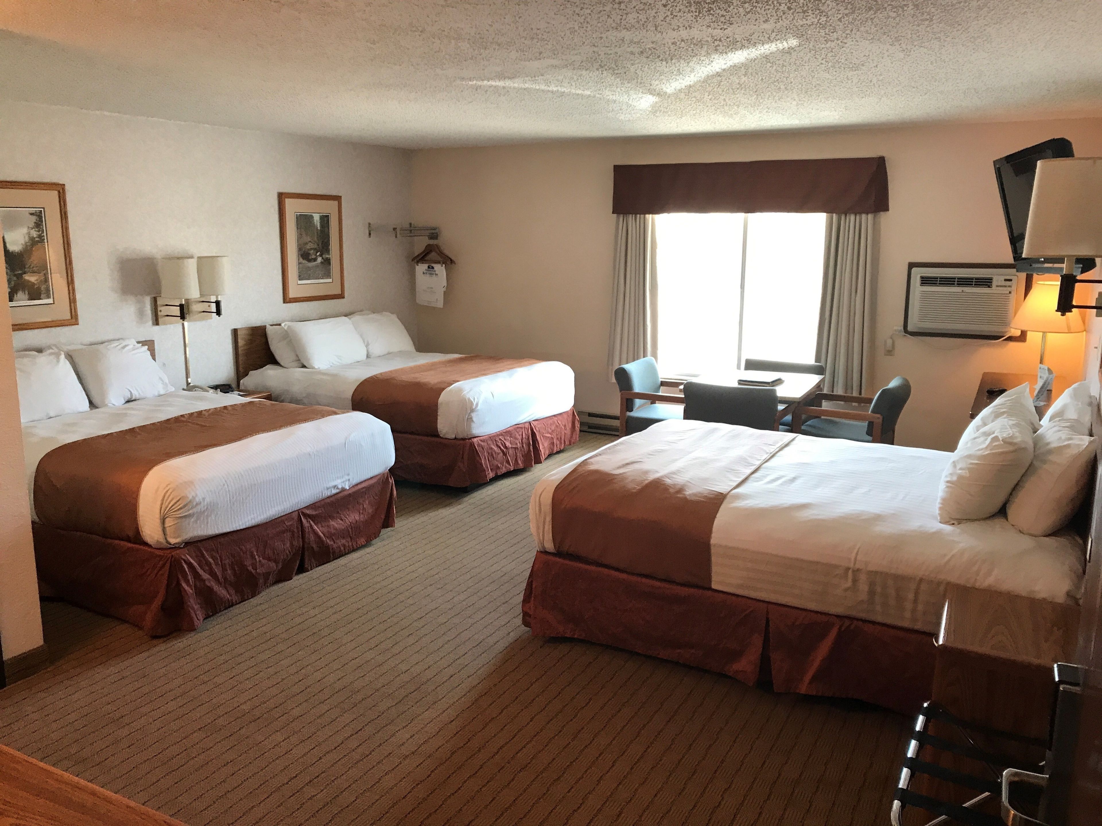 Habitación de hotel con dos camas, un escritorio, una silla y un ventanal con cortinas.