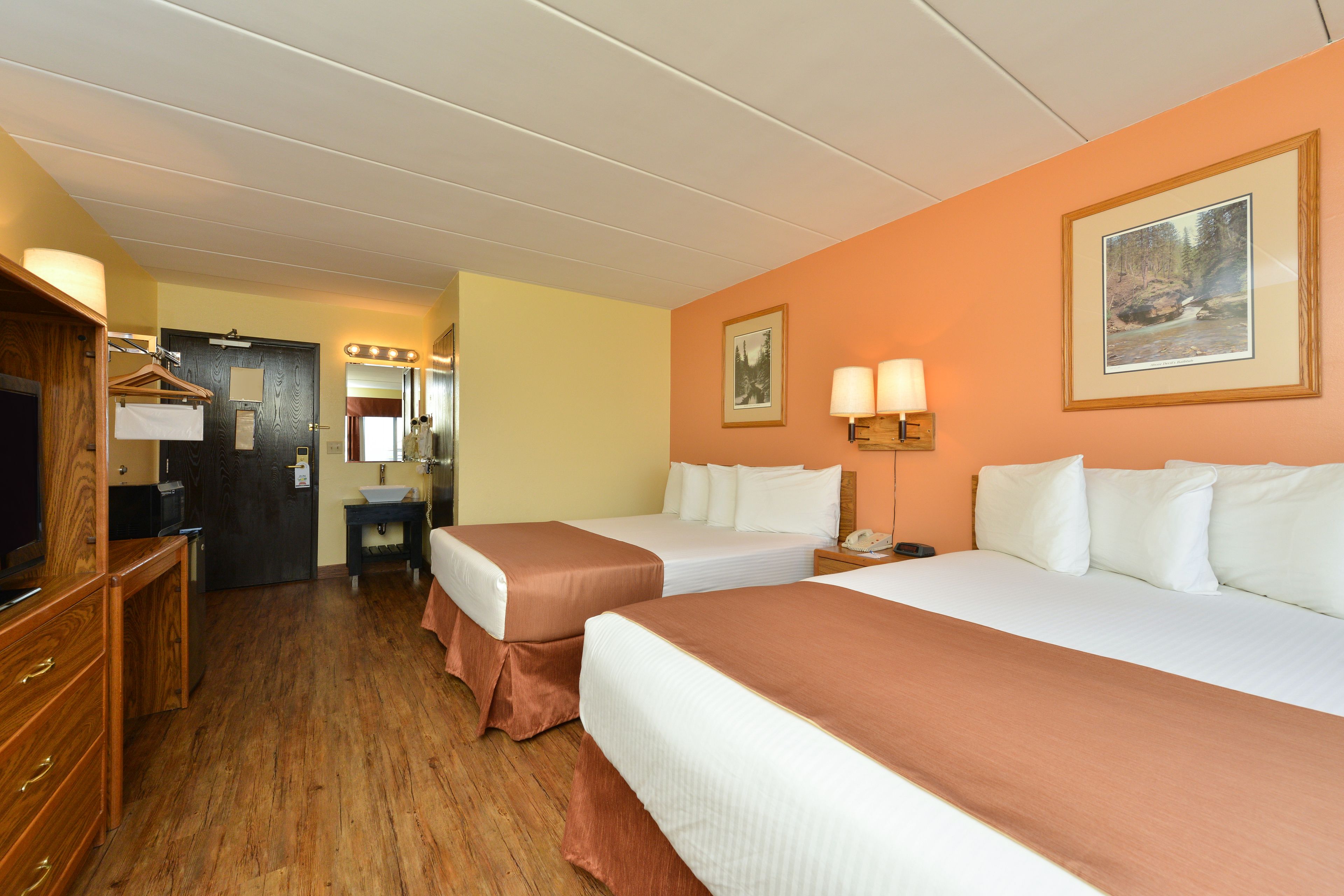 A hotel room with two beds, a wooden dresser, a mirror, a sink, and a framed picture on the wall.