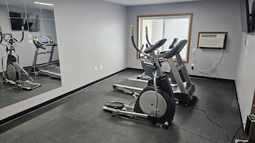 Une salle de sport équipée de tapis de course, de vélos elliptiques et d’un mur recouvert de miroirs.