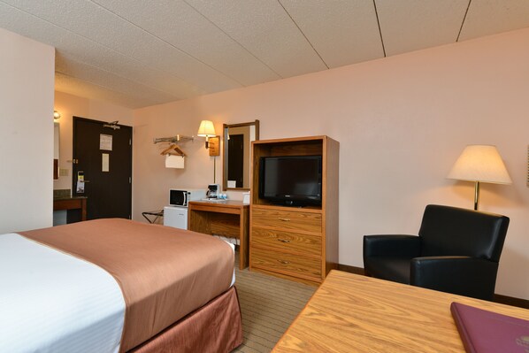 A hotel room with a bed, desk, chair, television, and a lamp.