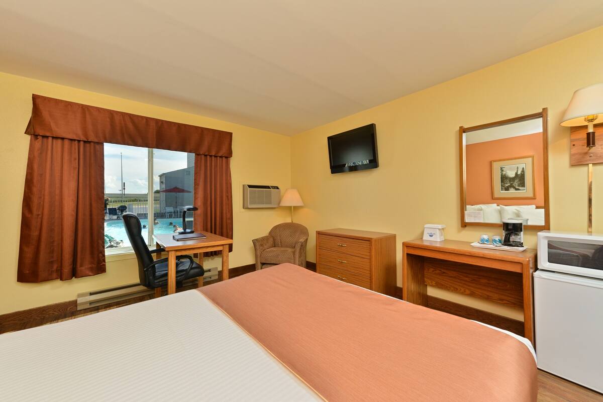Una camera d'albergo con un letto, una scrivania, una sedia, una cassettiera, televisione e vista sulla piscina.