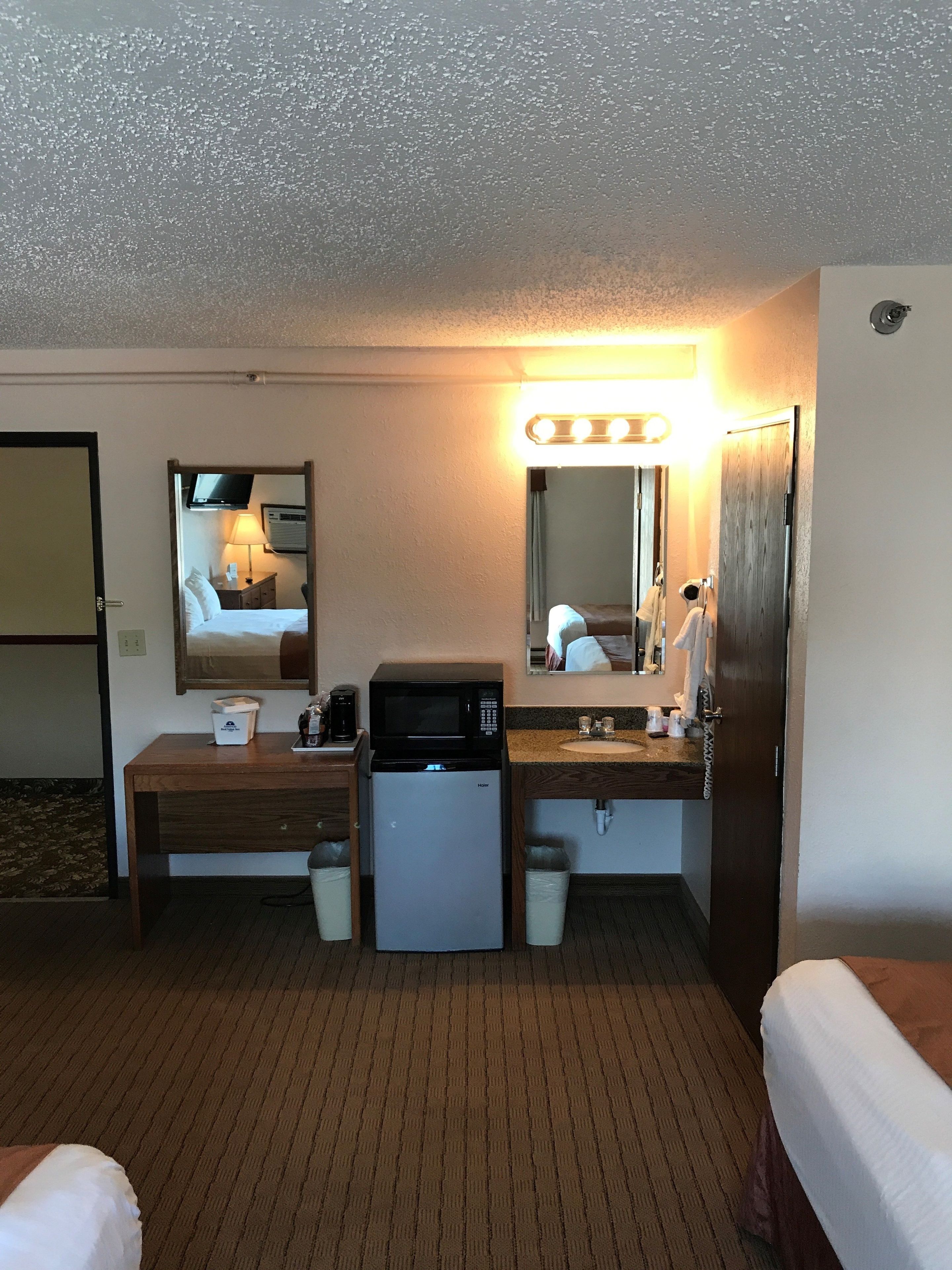 Quarto de hotel com cozinha compacta, cama, escrivaninha, espelho e banheiro.