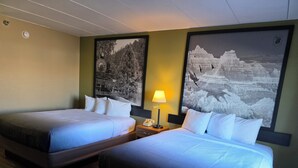 A hotel room with two beds, a nightstand with a lamp, and two large black-and-white landscape paintings on the walls.