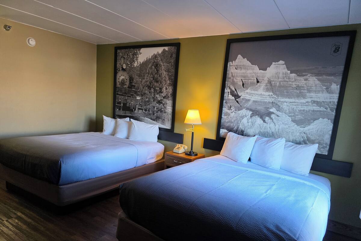 Una camera d'albergo con due letti, un comodino con una lampada e due grandi dipinti paesaggistici in bianco e nero alle pareti.