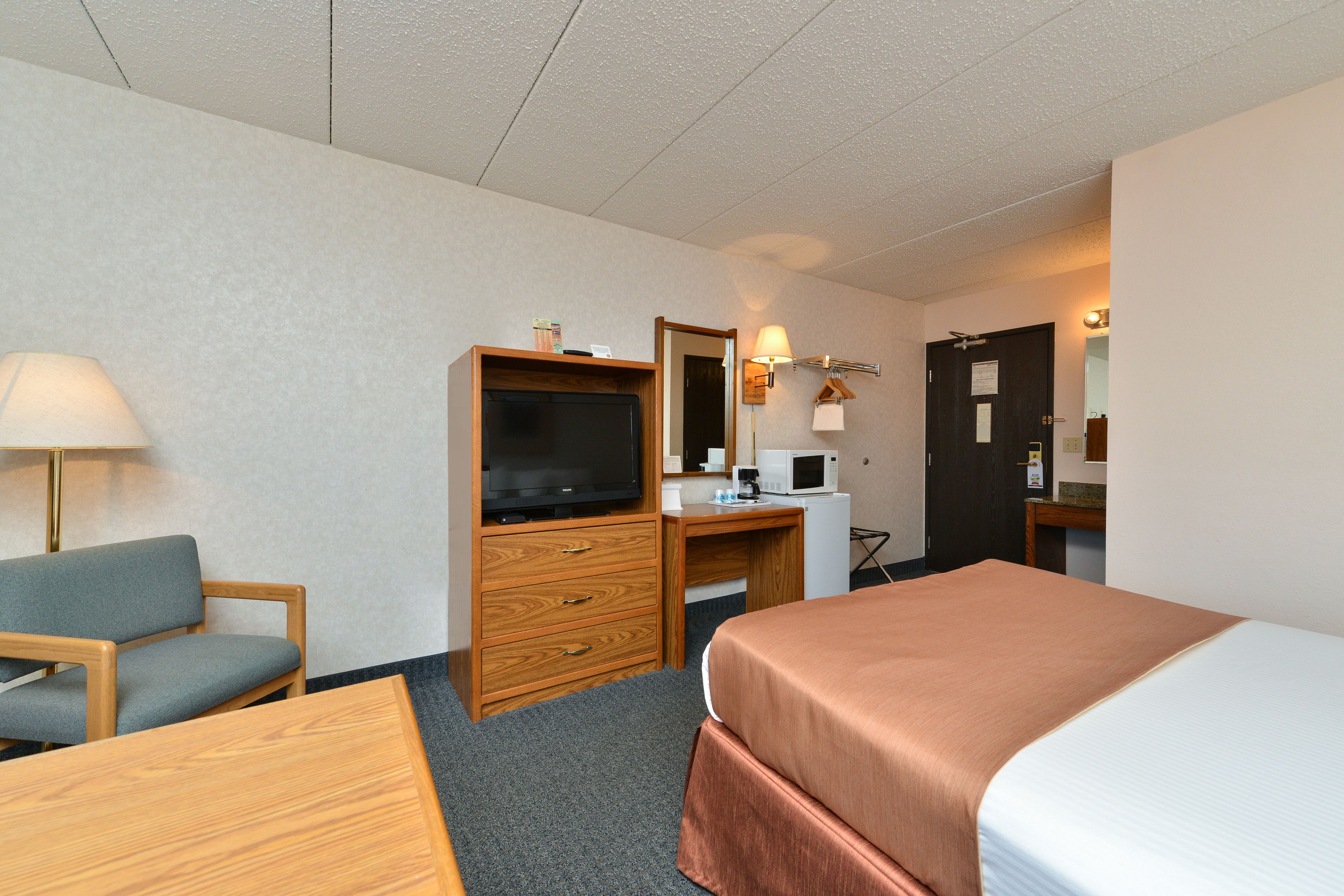 A hotel room with a bed, a desk with a computer, a television, a chair, and a lamp.