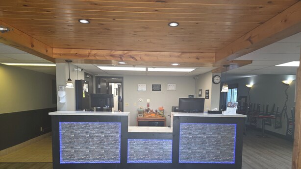 A reception area with a wooden ceiling, two reception counters with blue backlighting, a clock, and a doormat with a logo.