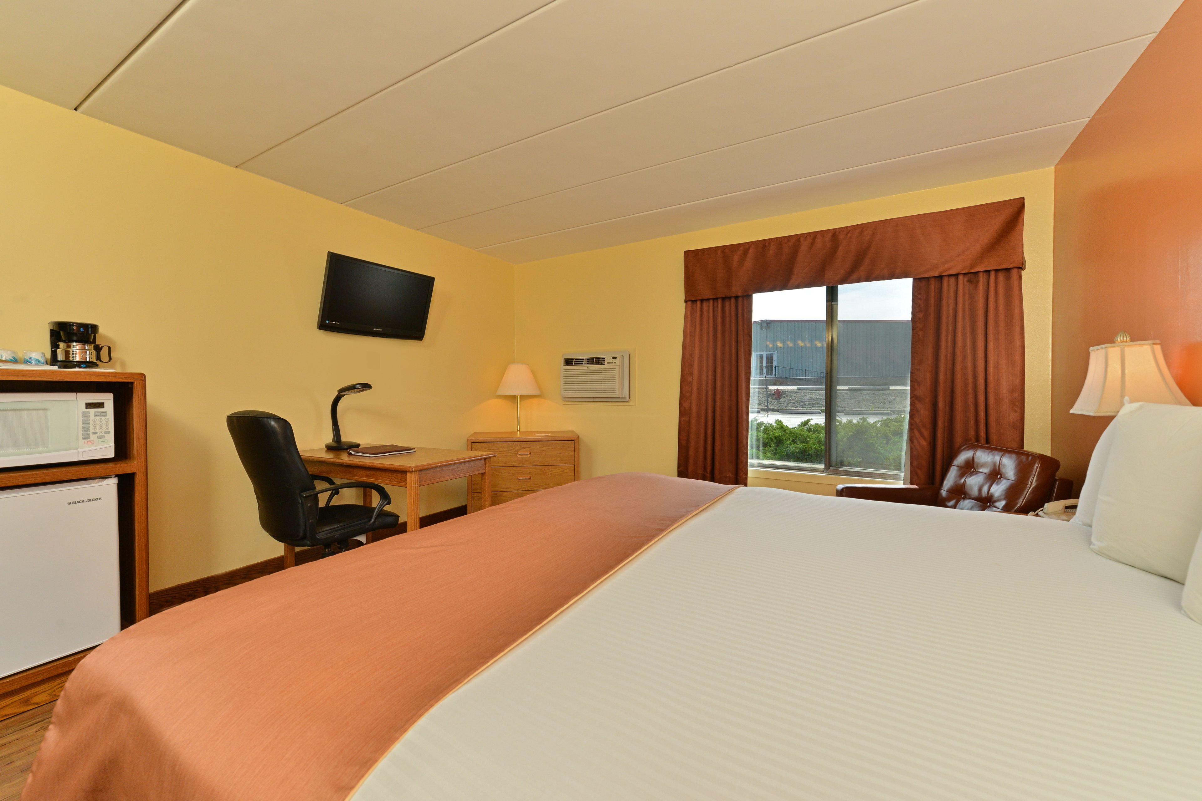 A hotel room with a bed, desk, chair, TV, and a window with curtains.