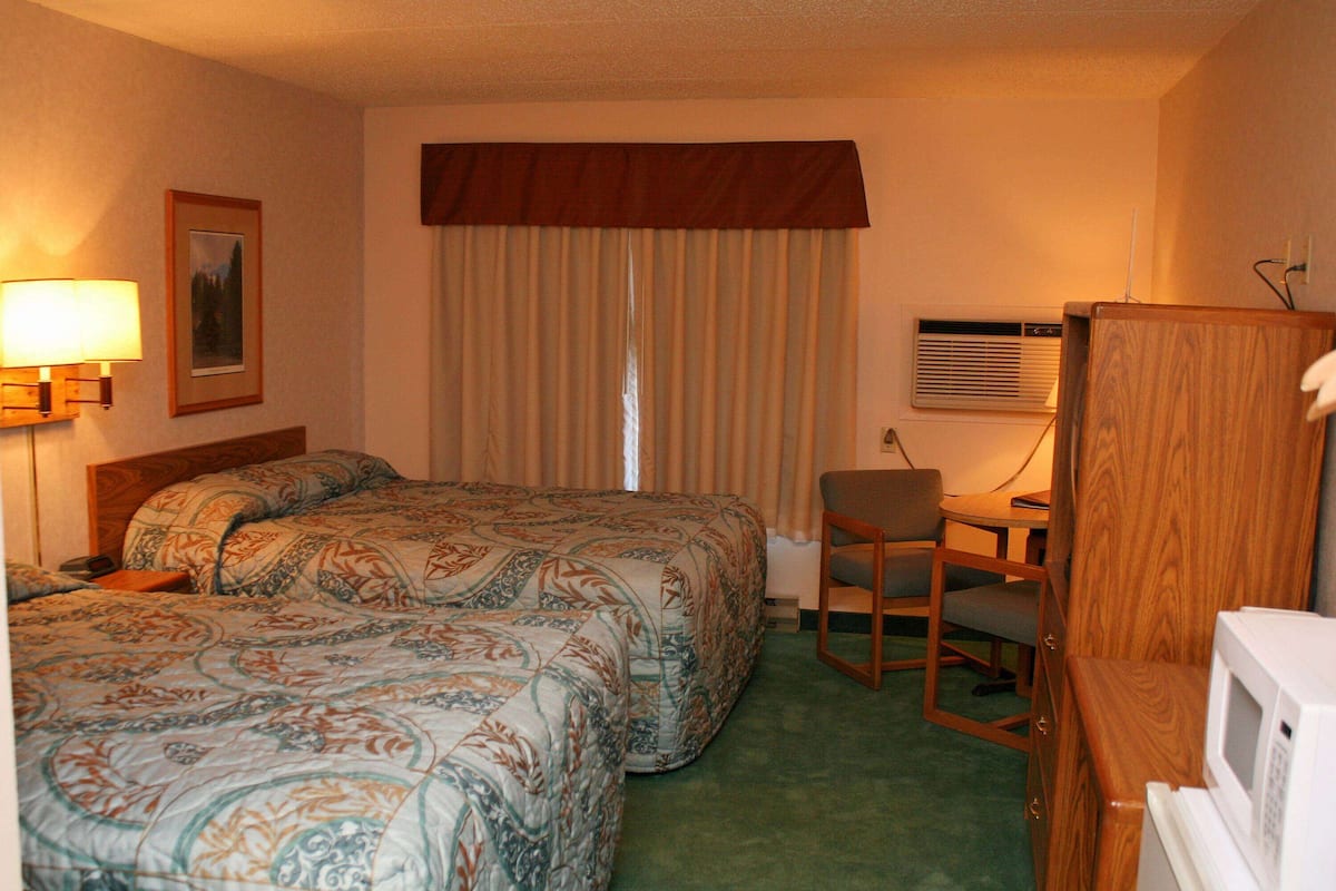 Una camera d'hotel con un letto grande, una scrivania con sedia, una lampada, un condizionatore e una televisione.